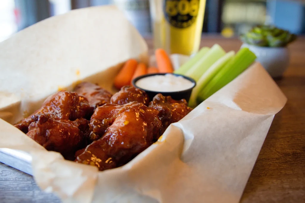 Glossy chicken wings, carrot, celery, and dip in metal tray.
