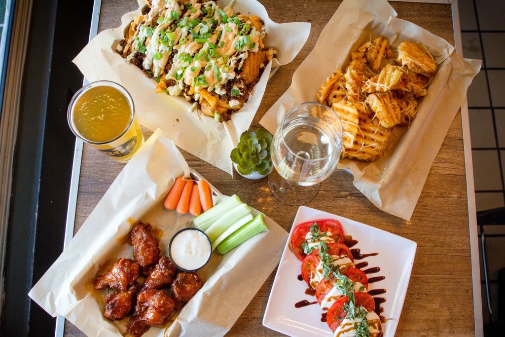 Overhead rustic table with loaded fries, chicken wings, Caprese salad, and drinks.