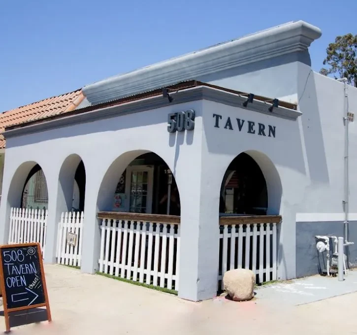 Stucco exterior of 508 TAVERN building, three archways, picket fence patio.
