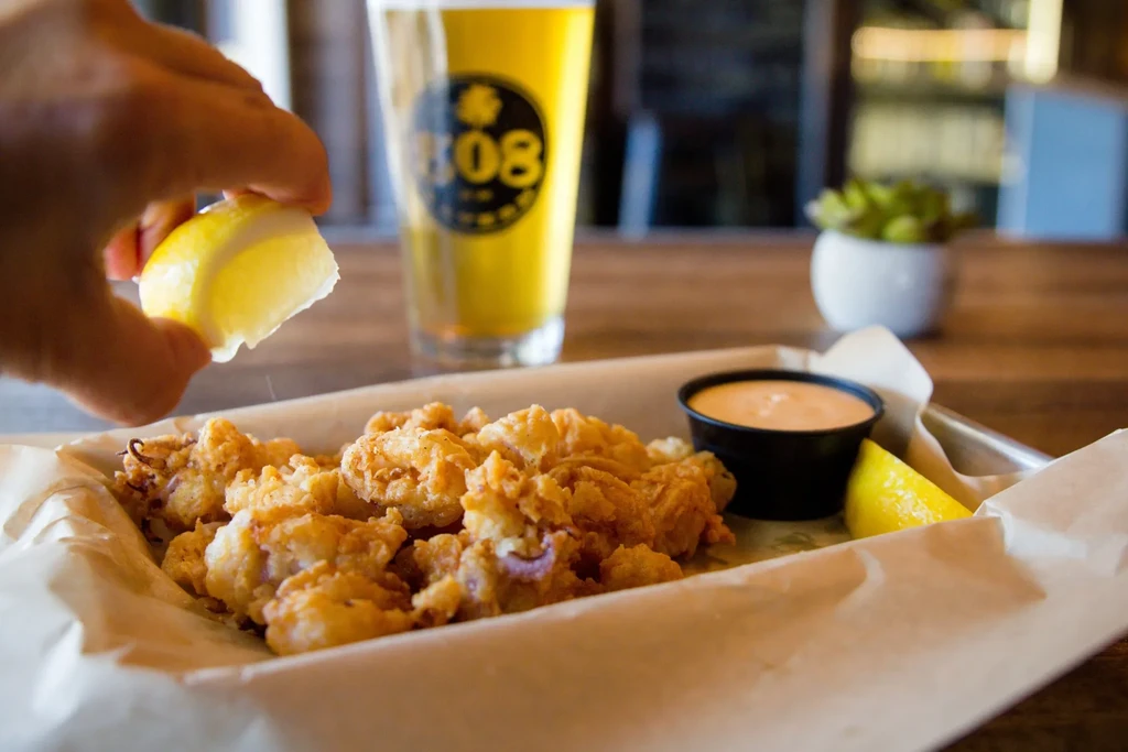Hand squeezing lemon over fried calamari with dipping sauce.