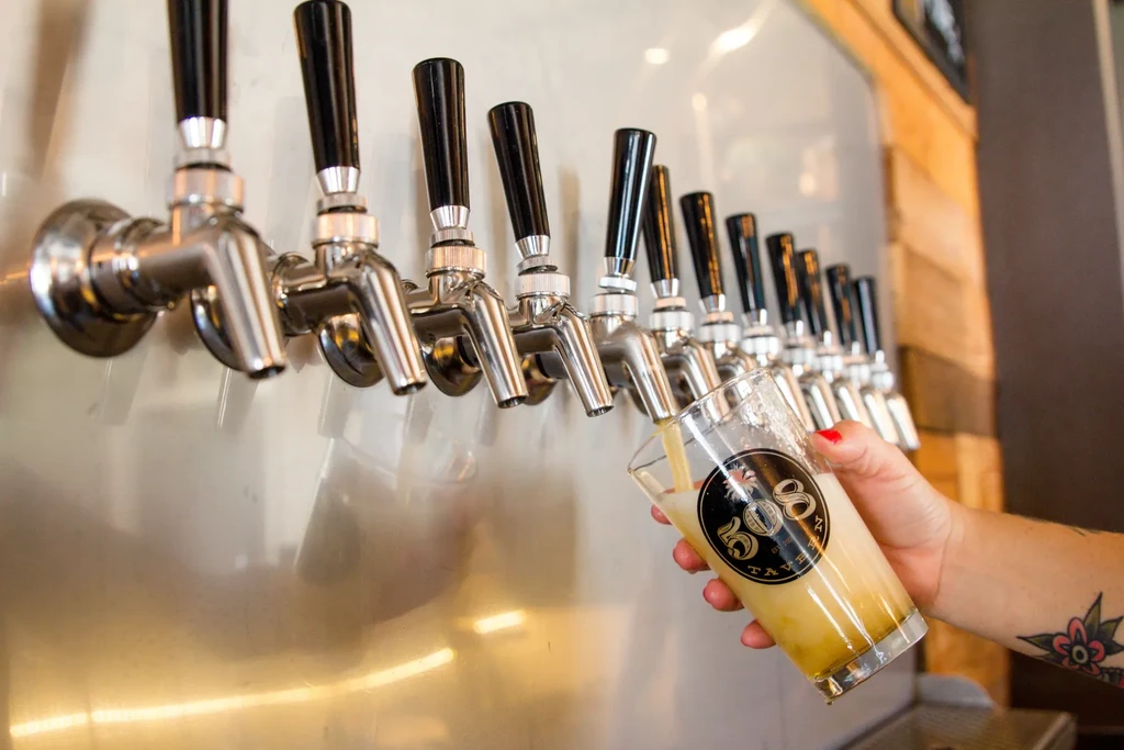 Hand with red nails pouring beer from chrome tap into a glass.