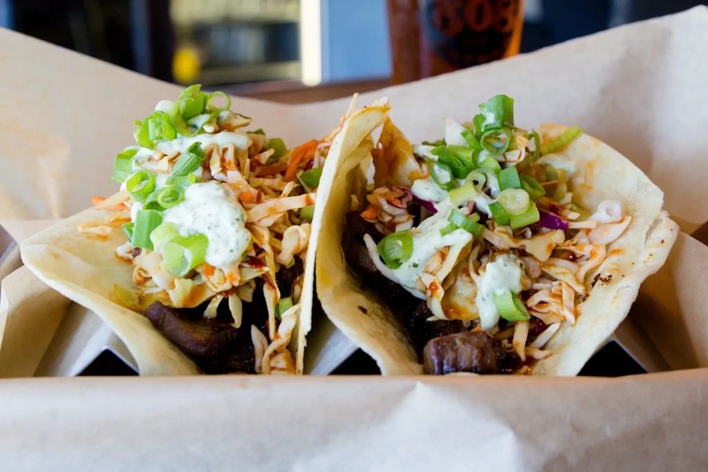 Two tacos with dark meat, coleslaw, sauce, and green onions.