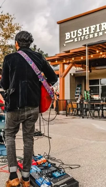 Musician playing red electric guitar outside Bushfire Kitchen restaurant.
