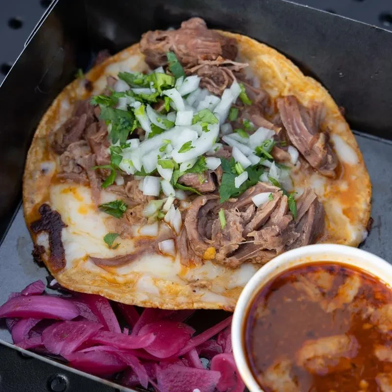 Quesabirria taco with meat, cheese, onions, cilantro, consommé, pickled onions.