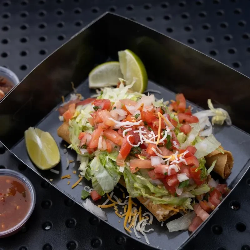 Takeout container with rolled tacos, lettuce, pico de gallo, cheese, lime, and salsa.