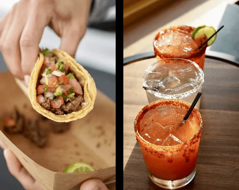 Hand holding a taco next to three cocktails on a wooden surface.