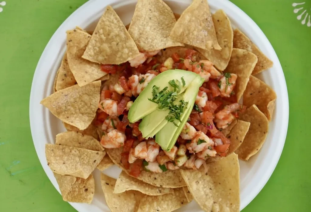 Shrimp ceviche with avocado and tortilla chips on a lime-green surface.