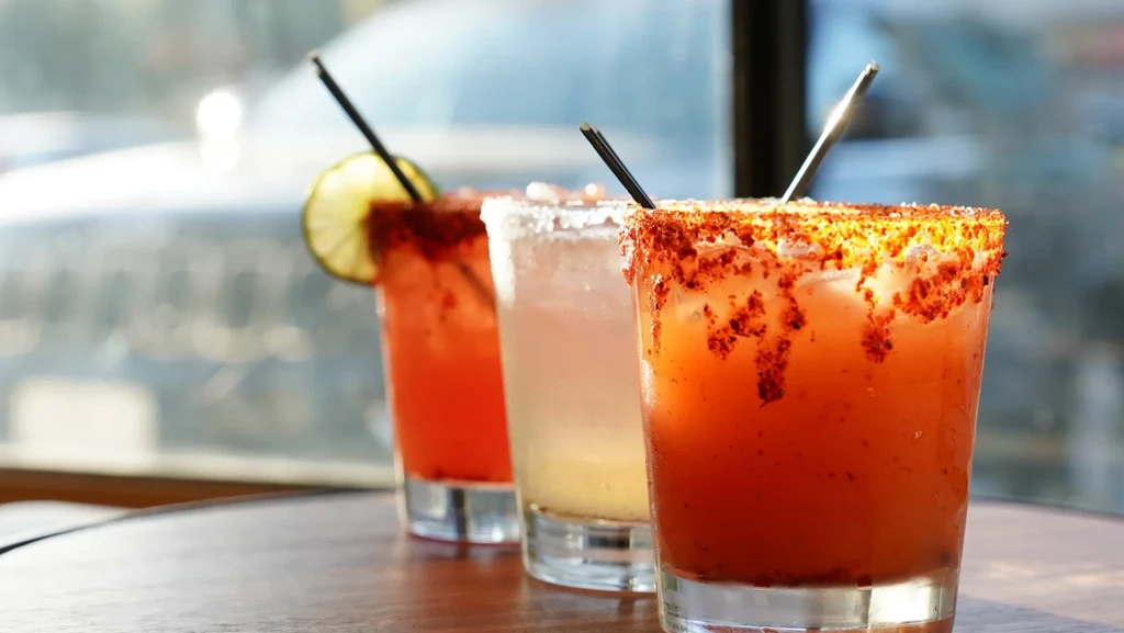 Three colorful, ice-filled drinks with spiced and salted rims on a table.