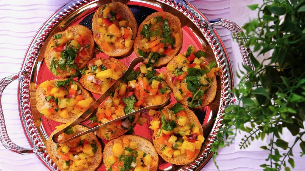 Top-down view of vibrant bruschetta on ornate silver platter with tongs.