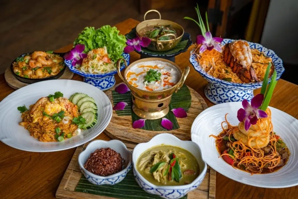 Vibrant spread of Thai dishes with seafood, orchids, and brass pots.