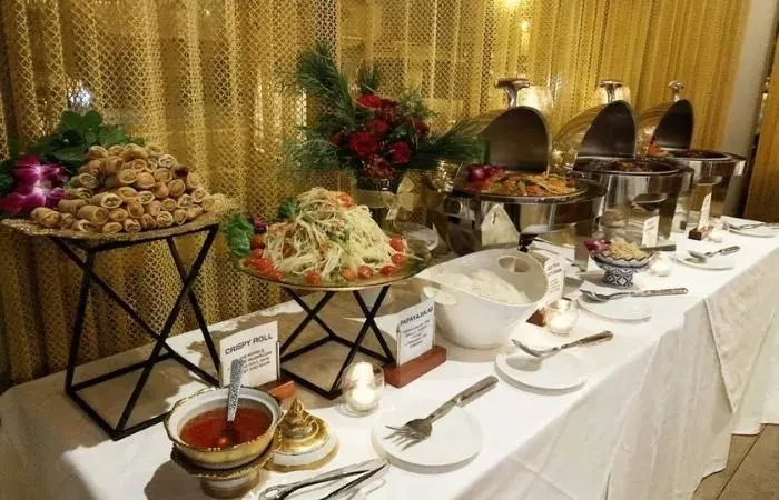 Buffet table with crispy rolls, papaya salad, chafing dishes, golden backdrop.