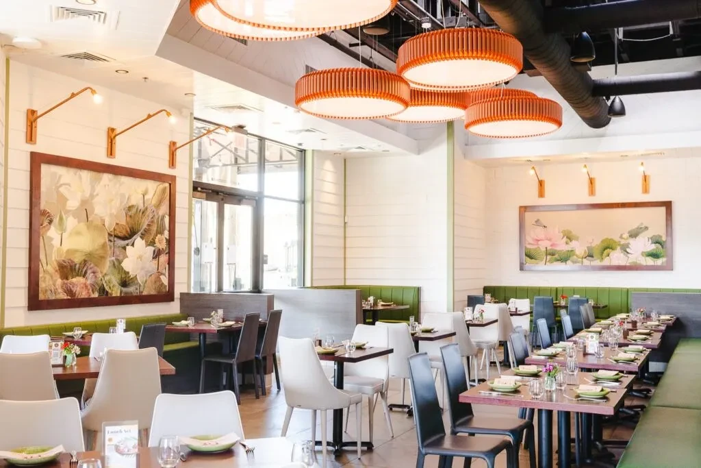 Modern restaurant dining area with green banquettes, lotus art, and warm lighting.