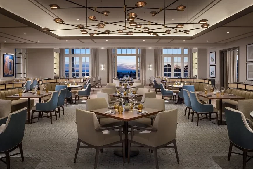Elegant, empty restaurant dining room with modern chandelier and set tables.