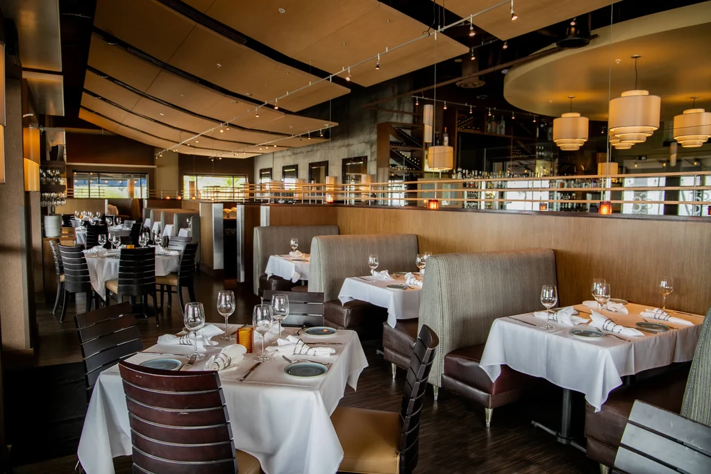 Modern, upscale restaurant interior, empty, with immaculately set tables and bar.