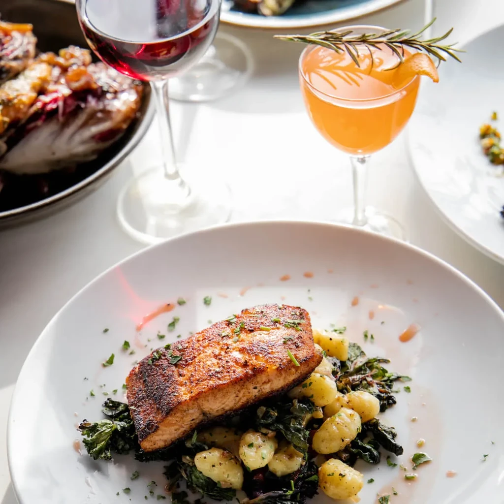 Upscale dining table with seared salmon, gnocchi, wine, and cocktails.