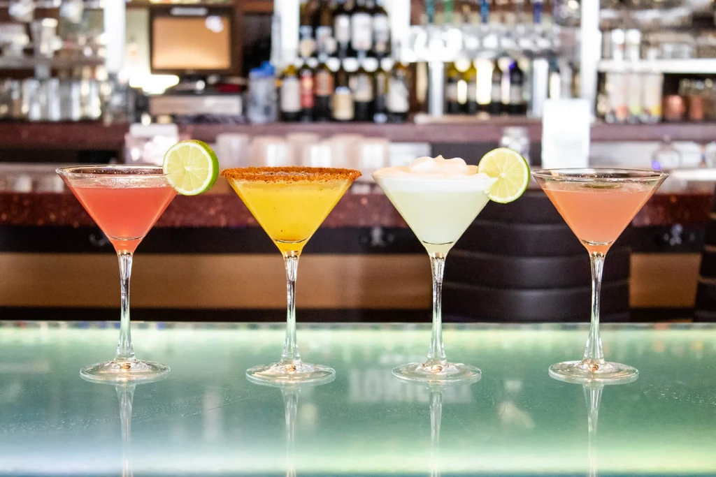 Four colorful martini cocktails in a row on a glowing bar.