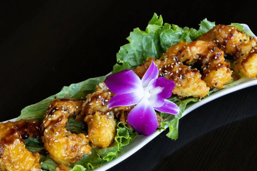 Fried food with dark sauce, sesame seeds, lettuce, and orchid garnish.