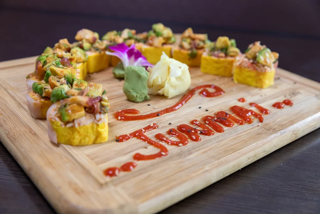 Yellow-wrapped sushi rolls with avocado, seafood, and "Tsunami" written on a board.