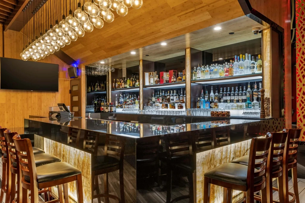 Modern bar with backlit counter, stocked backbar, and spherical chandelier.