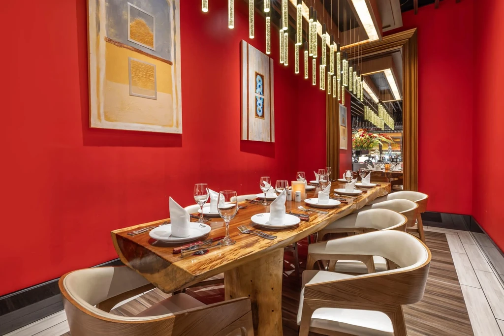 Red-walled private dining room with long wooden table and unique chandelier.