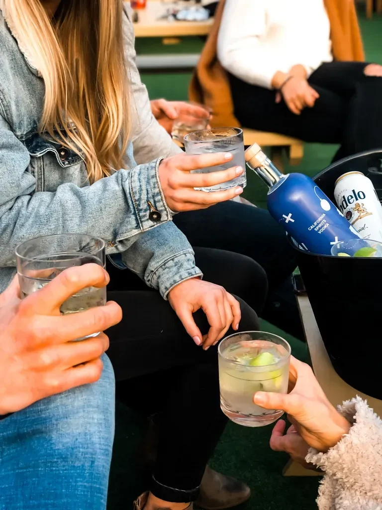 Outdoor patio: people hold iced drinks; cooler shows vodka and beer.