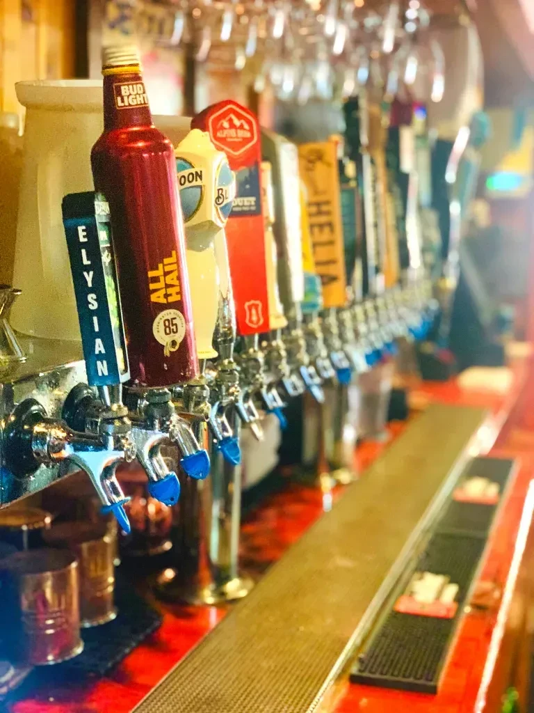 Close-up of beer taps: 'ALL HAIL' and 'ELYSIAN' in sharp focus.