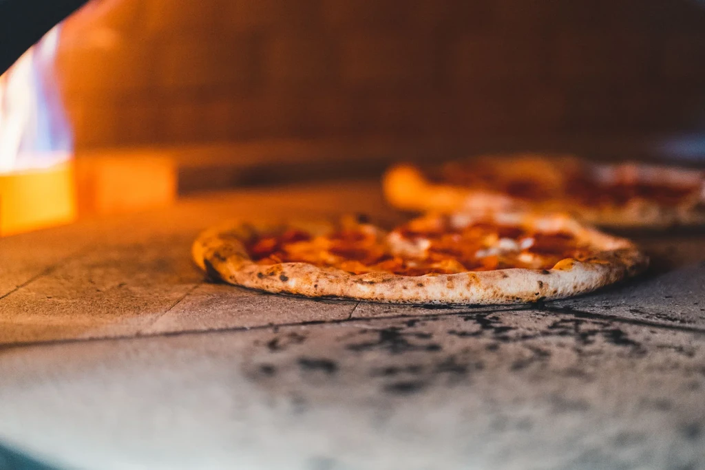 Two pizzas baking inside a traditional stone oven with flame.