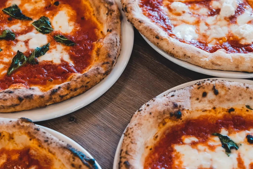 Four Neapolitan pizzas with charred crusts, sauce, and cheese on wood.