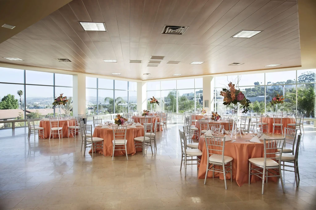Modern event hall with salmon-draped tables, autumn flowers, and scenic windows.