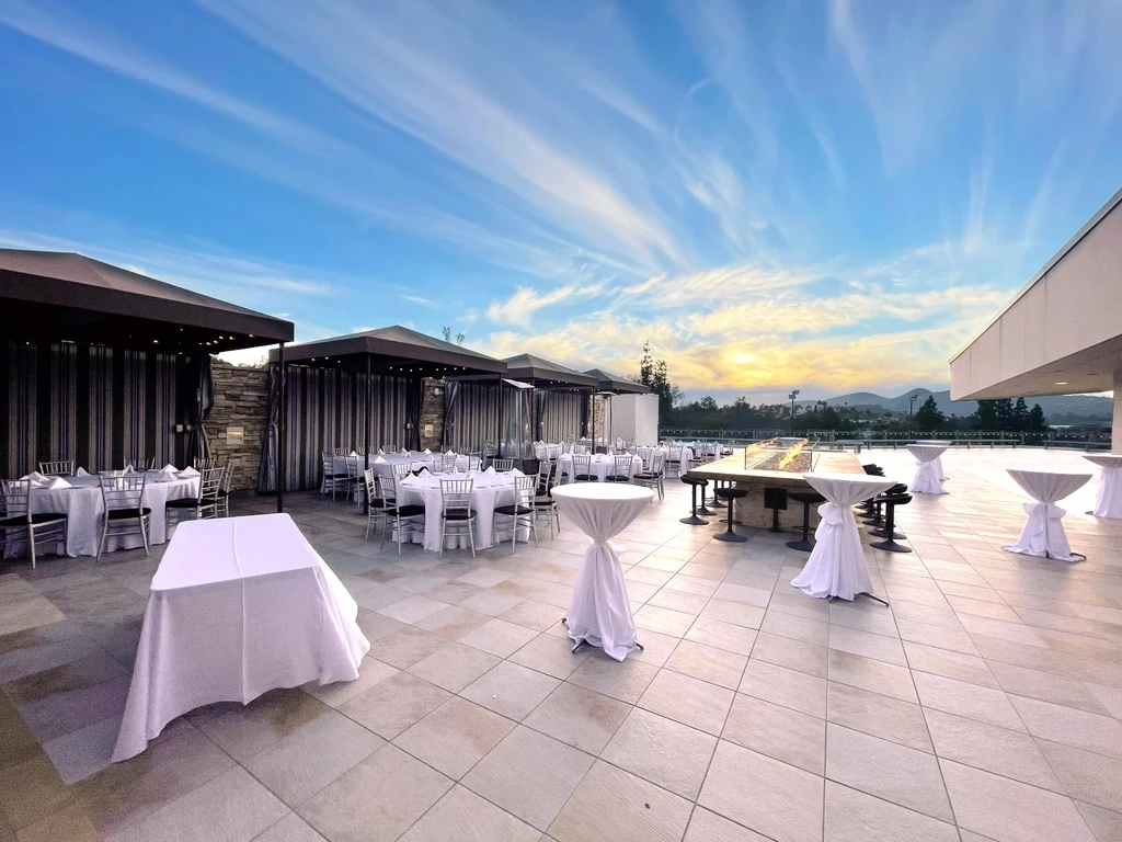 Outdoor patio with dining tables, fire pit, and cabanas at sunset.