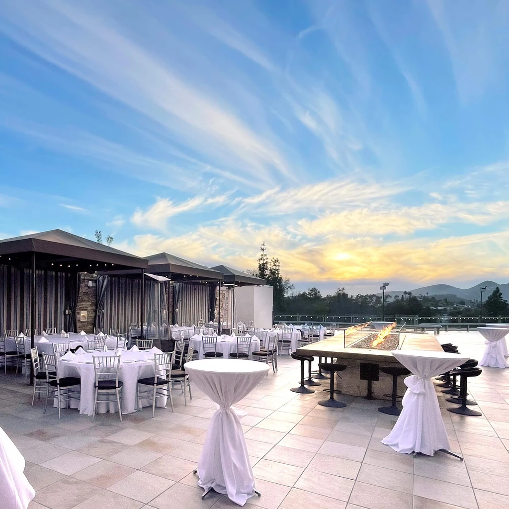 Outdoor event space with tables, fire pit, cabanas under sunset sky.