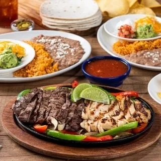 Sizzling steak and chicken fajitas with rice, beans, and tortillas.