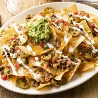Plate of nachos with cheese, beef, tomatoes, jalapeños, sour cream, guacamole.
