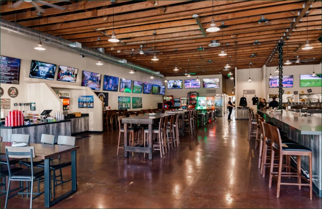 Spacious, modern casual restaurant interior with TVs, arcade games, and exposed beams.
