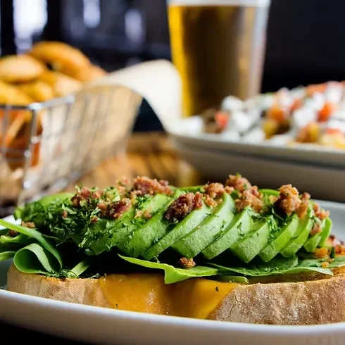 Avocado toast with bacon, spinach, and a yellow spread.