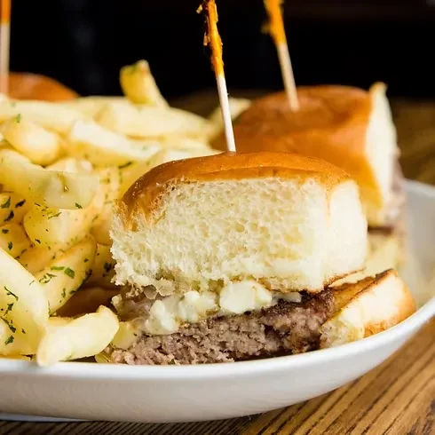 Two sliders with toothpicks and fries in a white bowl.