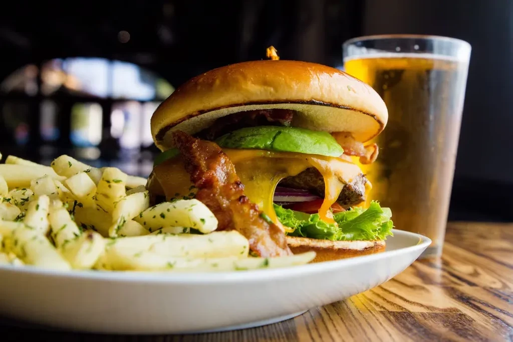Gourmet burger with fries and beer on a wooden table.