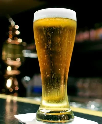 Pilsner glass with golden beer, white foam, and rising bubbles.