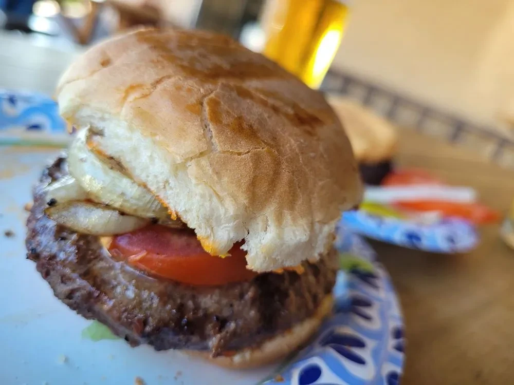 Hamburger with tomato and grilled onions on a disposable plate.