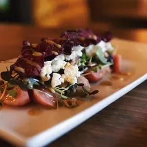 Plated dish with tomatoes, crumbled cheese, greens, and purple chips.