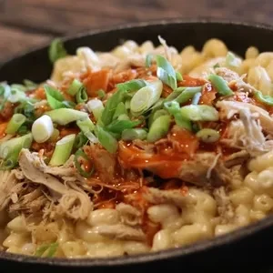Macaroni and cheese with shredded meat, orange sauce, and green onions.