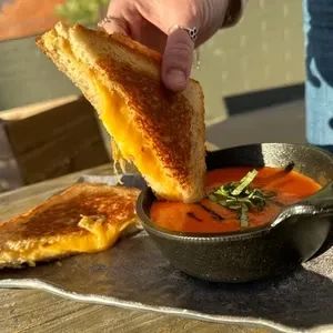 Hand dipping grilled cheese into tomato soup in a cast iron pot.