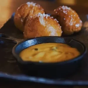 Three golden-brown pretzel bites with salt and a cheese dipping sauce.