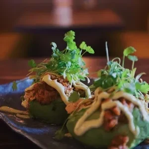 Avocado halves filled with meat, topped with sauce and green herbs.