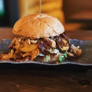 Gourmet burger with brioche bun, multiple patties, cheese, and bacon.
