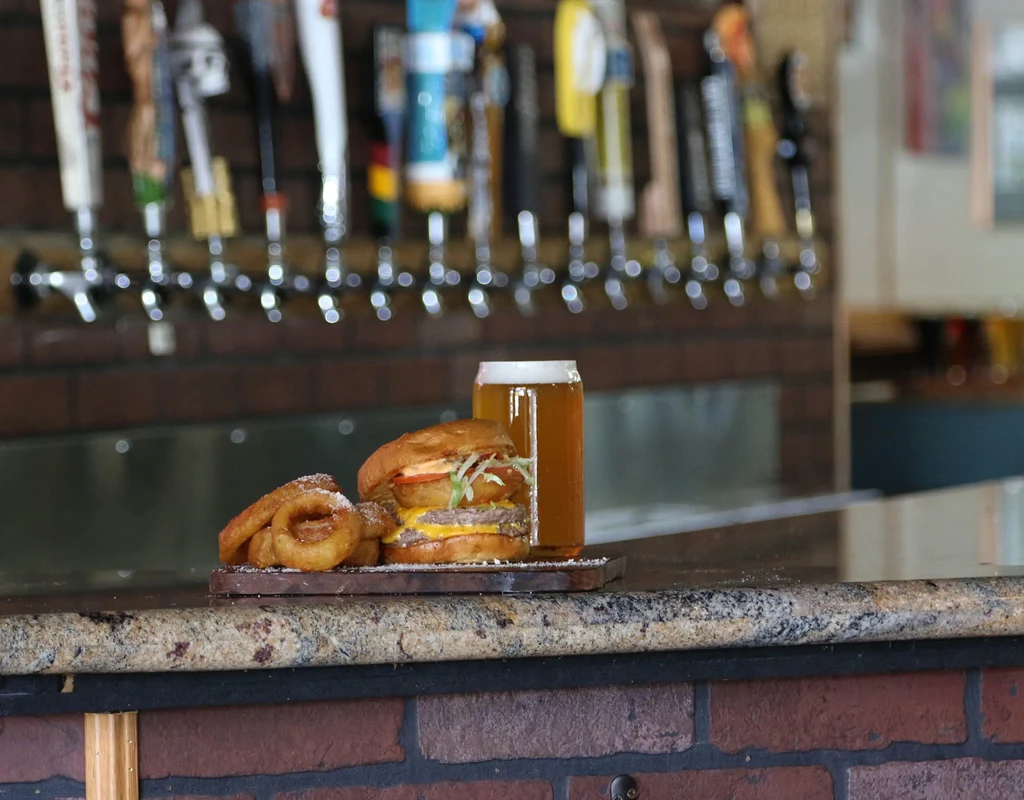 Double cheeseburger, crispy onion rings, and a beer at a bar.