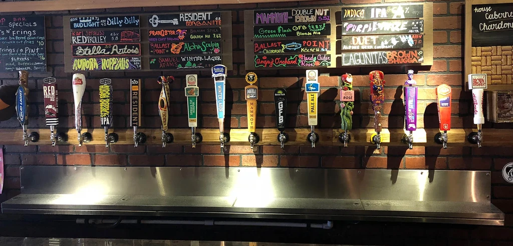 Nineteen beer taps and chalk menu boards against a rustic brick wall.