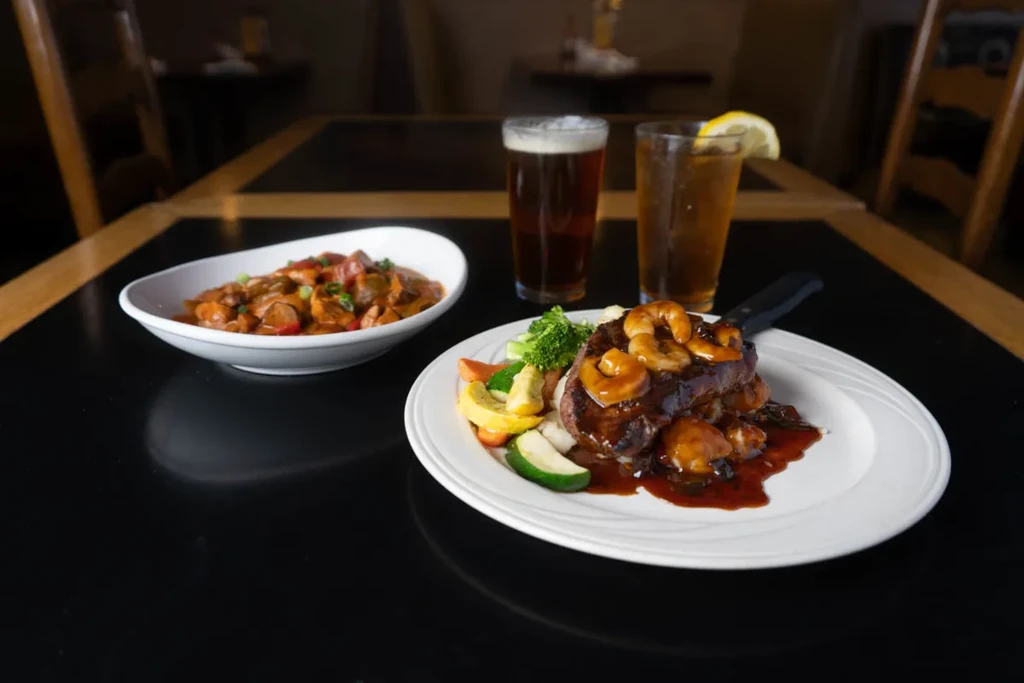 Restaurant table with stew, steak, beer, and iced tea.