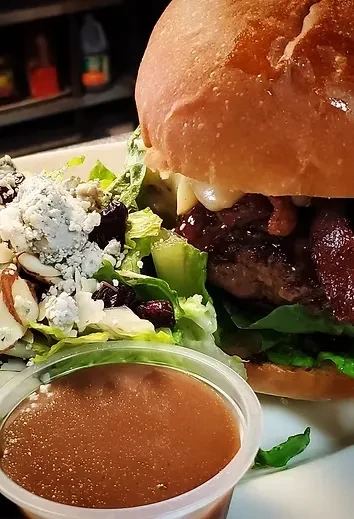 A gourmet burger, side salad with cranberries and blue cheese, and dipping sauce.