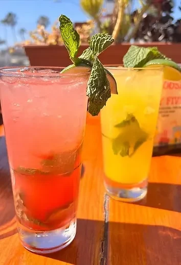 Red and yellow layered drinks with mint and lime on an outdoor table.